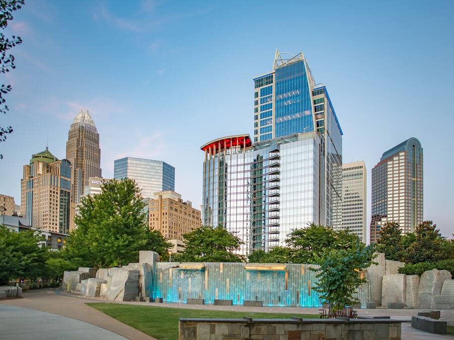 A cityscape with modern high-rise buildings, a central plaza with a water feature, and a clear sky.