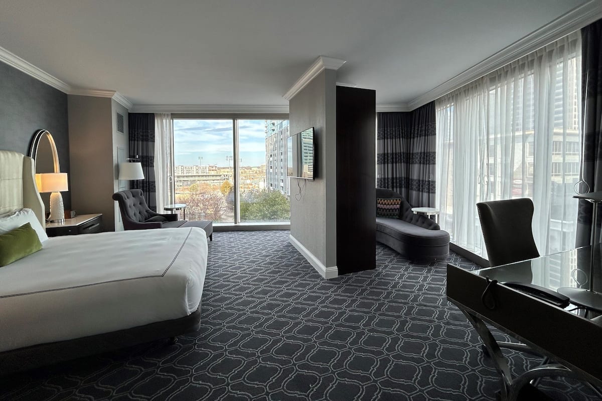 A hotel room with a large bed, a desk, a chair, a sofa, and a view of the city.