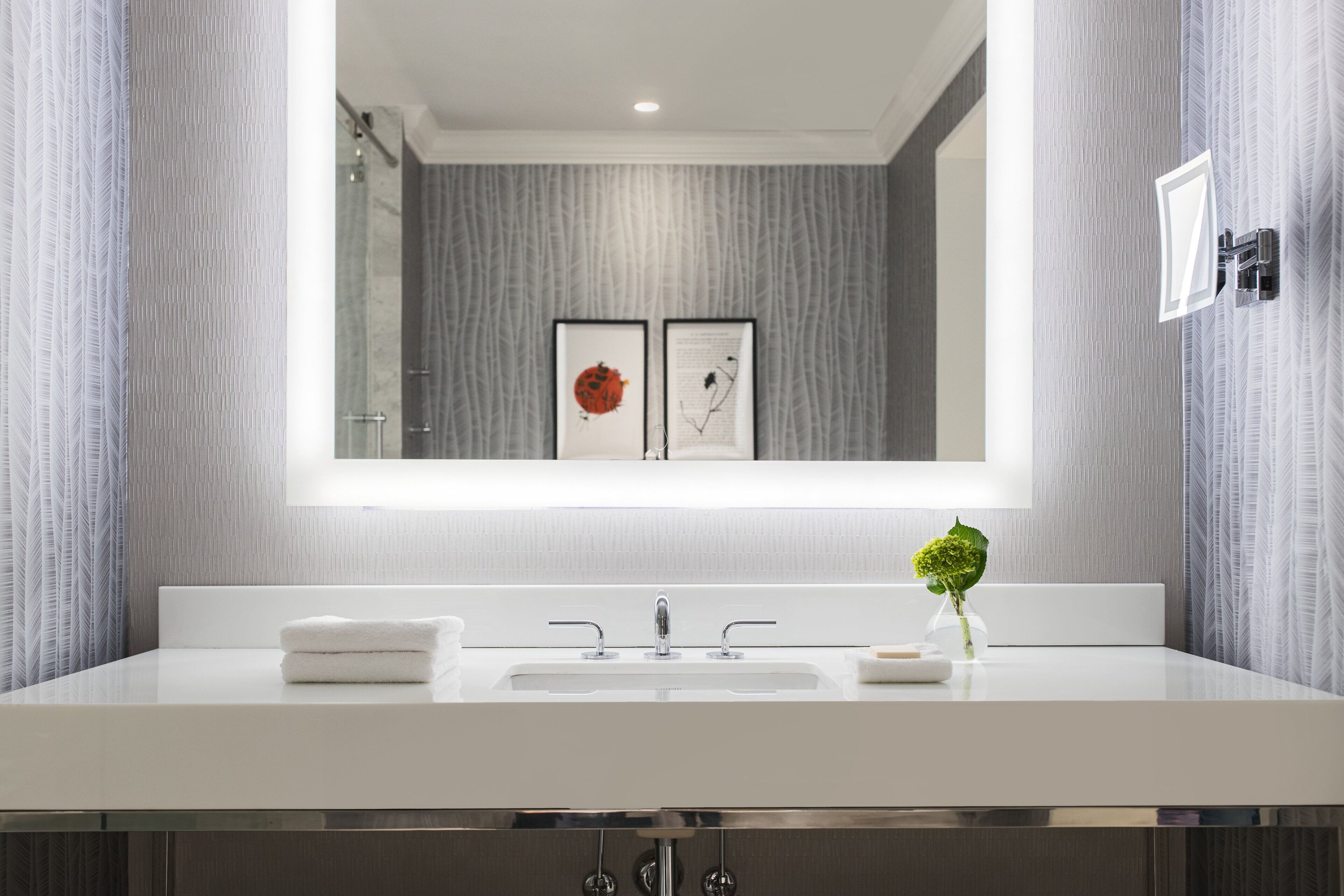 A modern bathroom with a large mirror, a white sink, and a small vase with a green plant.