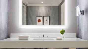 A modern bathroom with a large mirror, a white sink, and a small vase with a green plant.