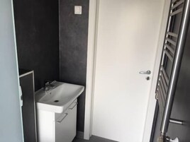 Un baño pequeño y funcional con un lavamanos blanco, un espejo y una puerta que da a la zona de la ducha.