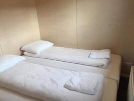 Una habitación con dos camas, cada una con ropa blanca de cama y almohadas, y una pared color beige.
