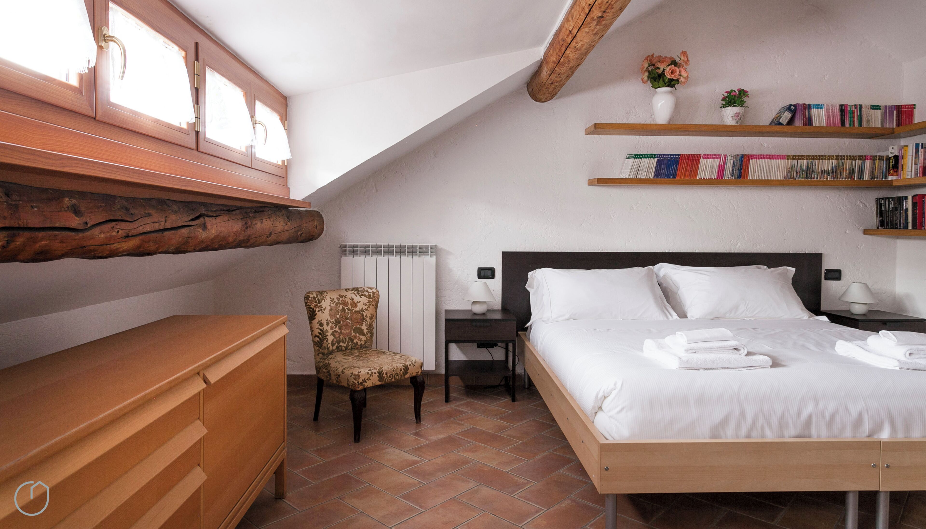 A bedroom with a wooden bed, a chair, a nightstand, a bookshelf, and a radiator.