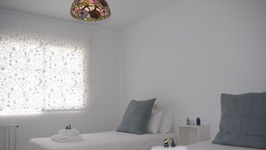 A minimalist bedroom with two beds, a radiator, a nightstand, and a decorative stained glass light fixture. - La Casa de Manuel (Portomarin)