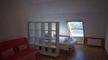 Una habitación con un sofá rojo, una cama con cabecera de madera, un panel blanco y una ventana con vistas al exterior.