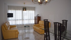 A spacious living room with a yellow sofa, a glass dining table, and a chandelier. - La Casa de Manuel (Portomarin)