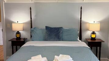 Un lit bien fait, recouvert d’une couverture bleue, avec deux oreillers et une pile de serviettes blanches posée sur le pied de lit. On y trouve deux tables de chevet avec des lampes et une tête de lit en bois.