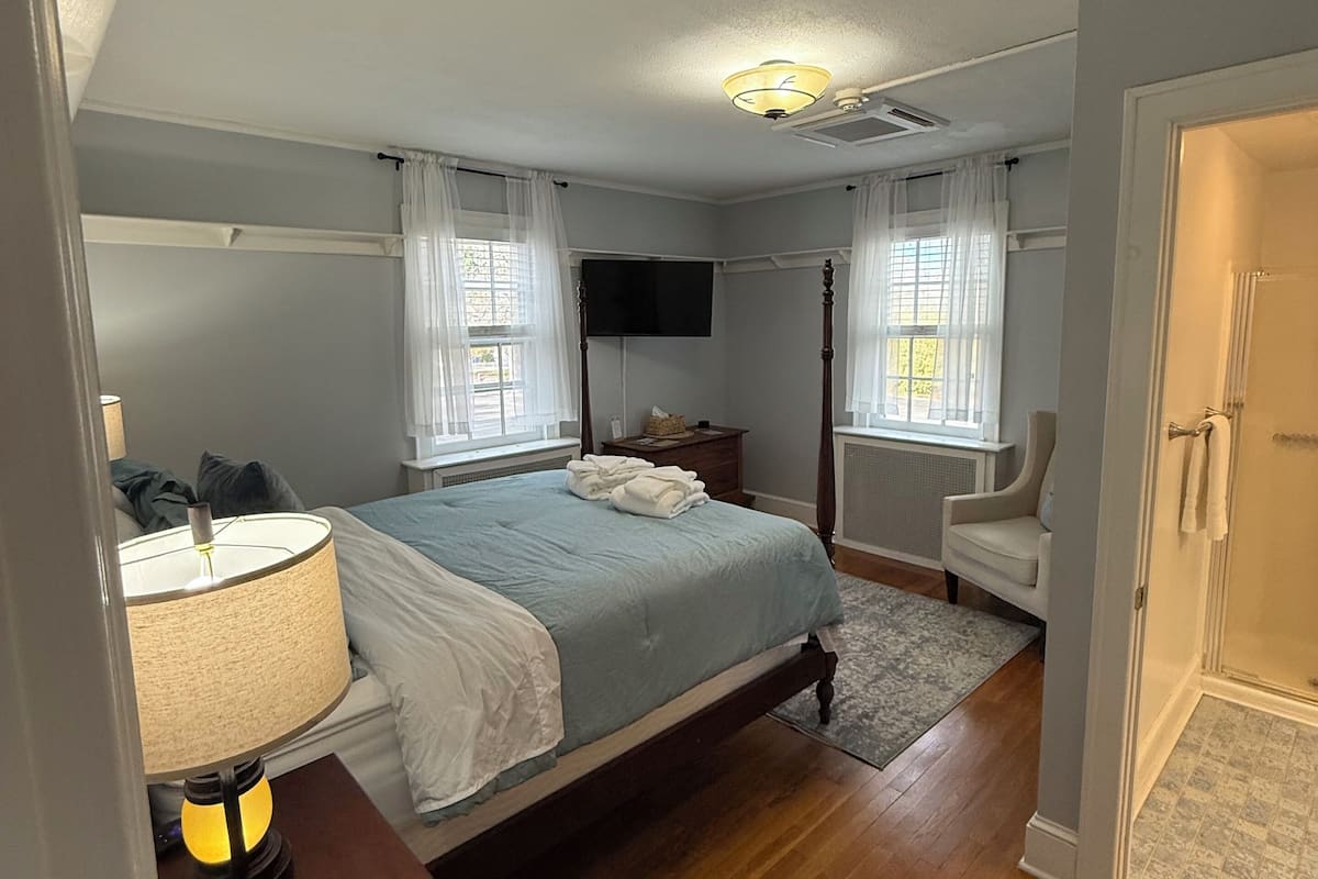 Quarto com cama, mesa de cabeceira, luminária e televisão na parede.