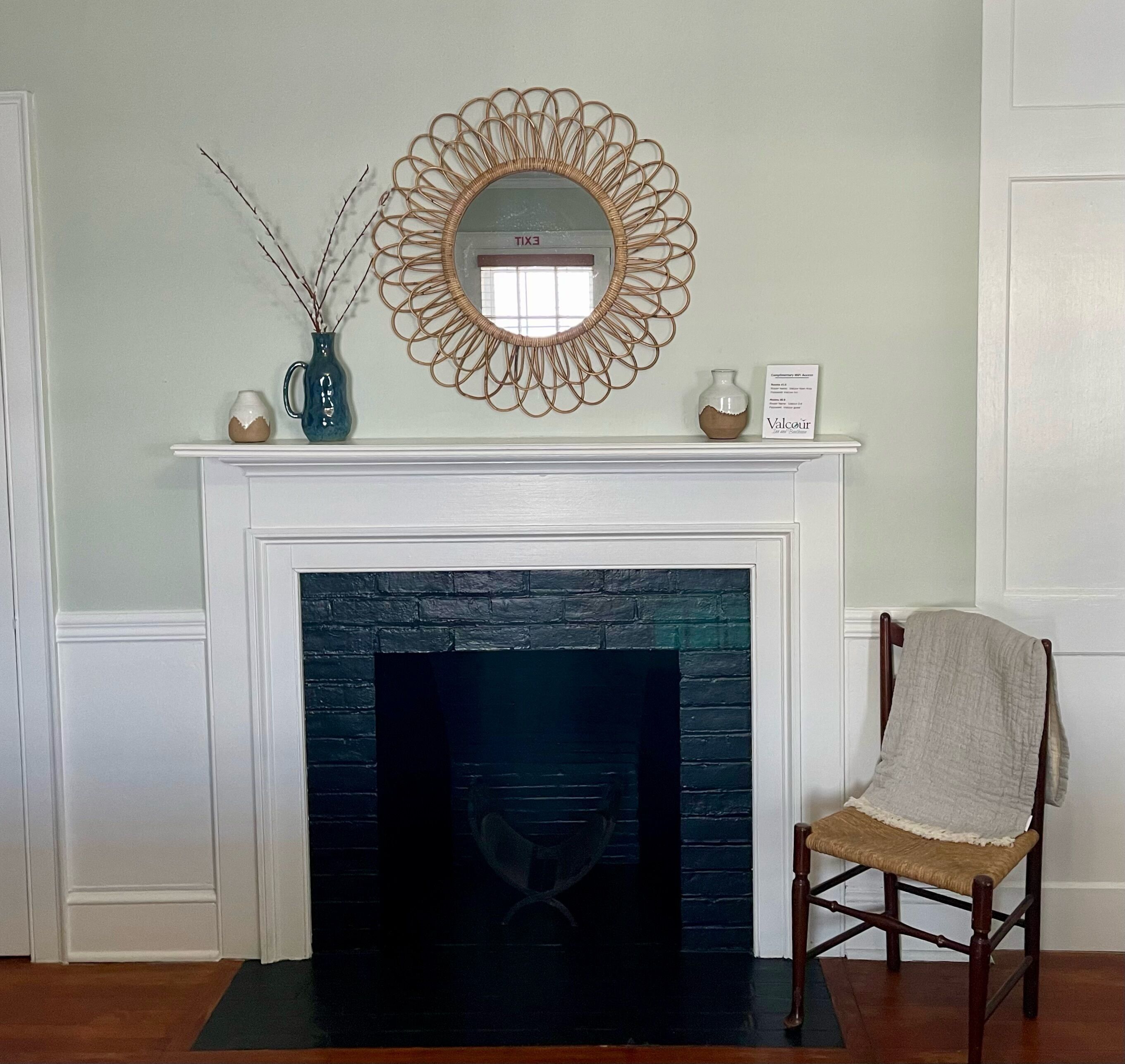 A fireplace with a black brick surround, a decorative mirror above it, and a chair to the right.