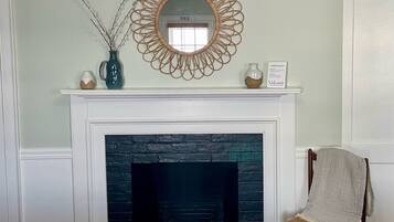 A fireplace with a black brick surround, a decorative mirror above it, and a chair to the right.