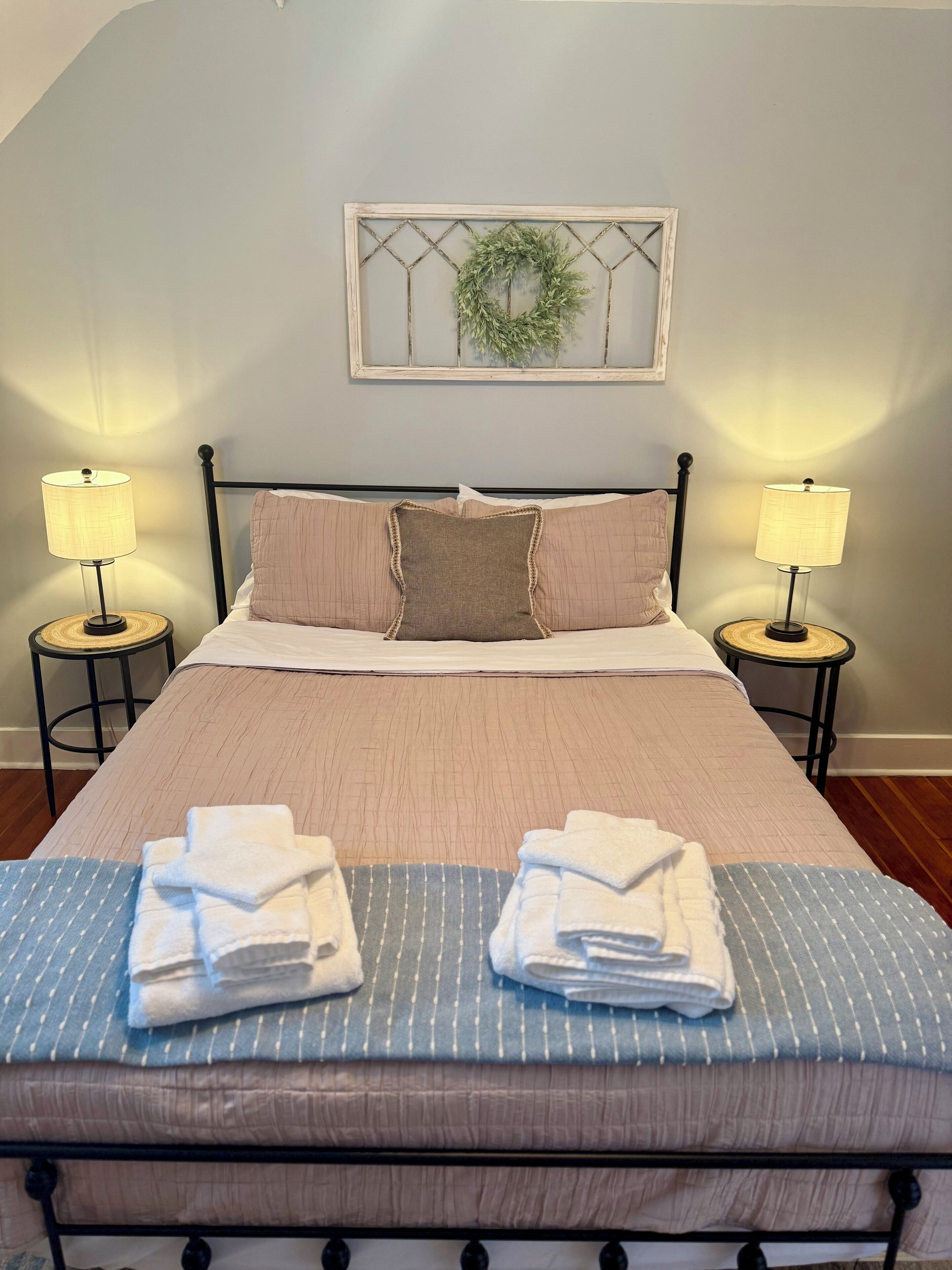 A neatly made bed with a beige and blue striped bedspread, two pillows, and two bedside lamps on matching nightstands.