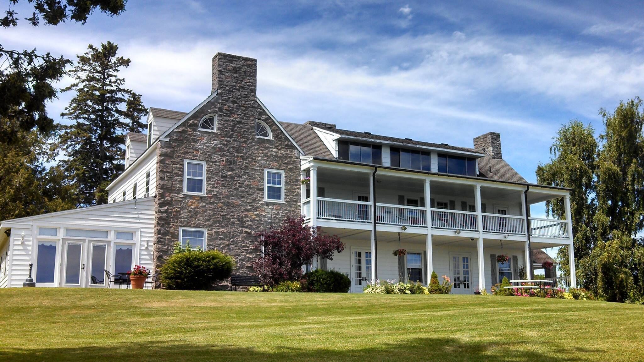 A two-story stone house with a covered porch and a second-story balcony.