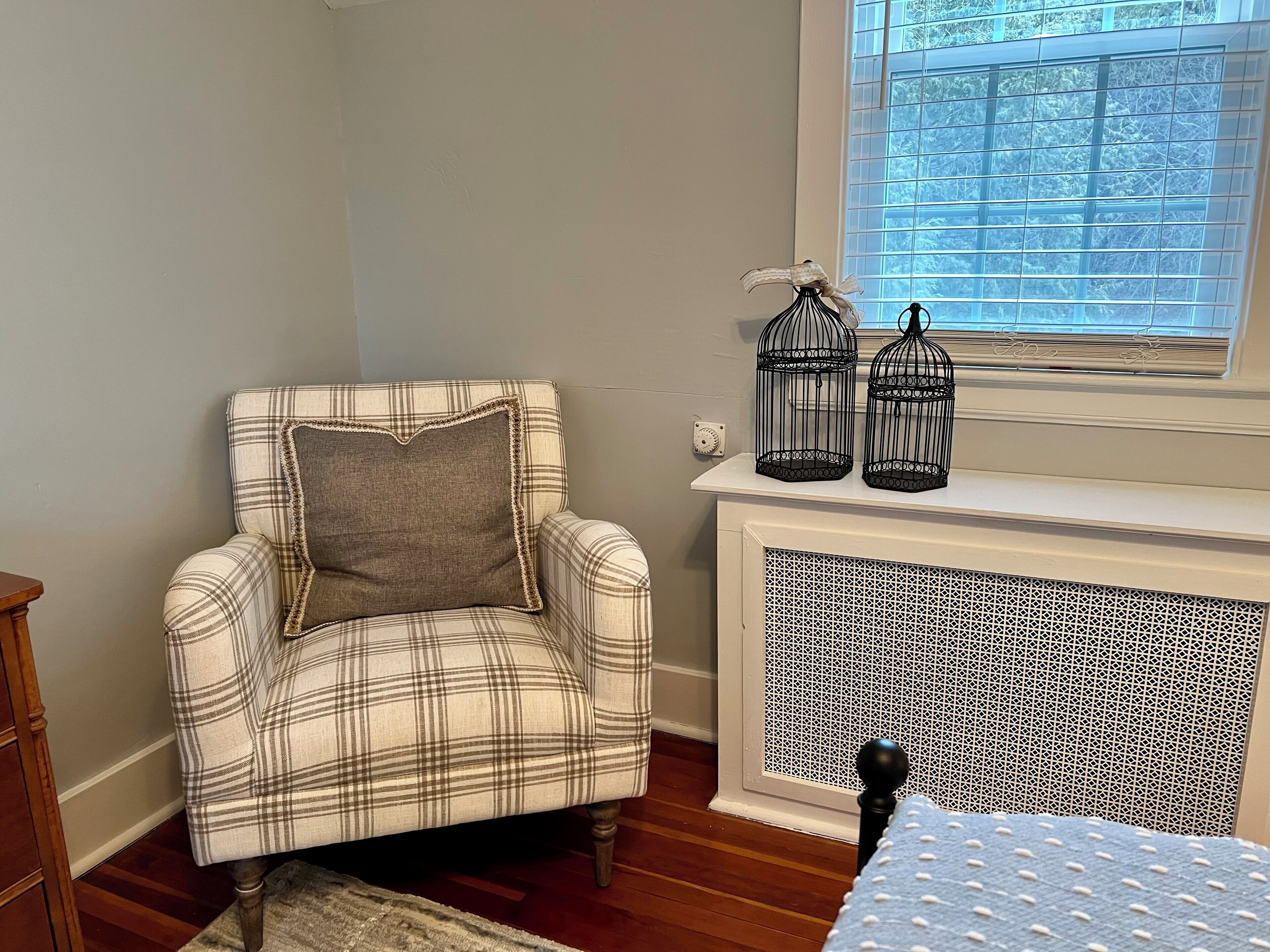 A plaid armchair with a pillow, a radiator, and two birdcages on a mantelpiece.