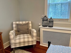 A plaid armchair with a pillow, a radiator, and two birdcages on a mantelpiece.