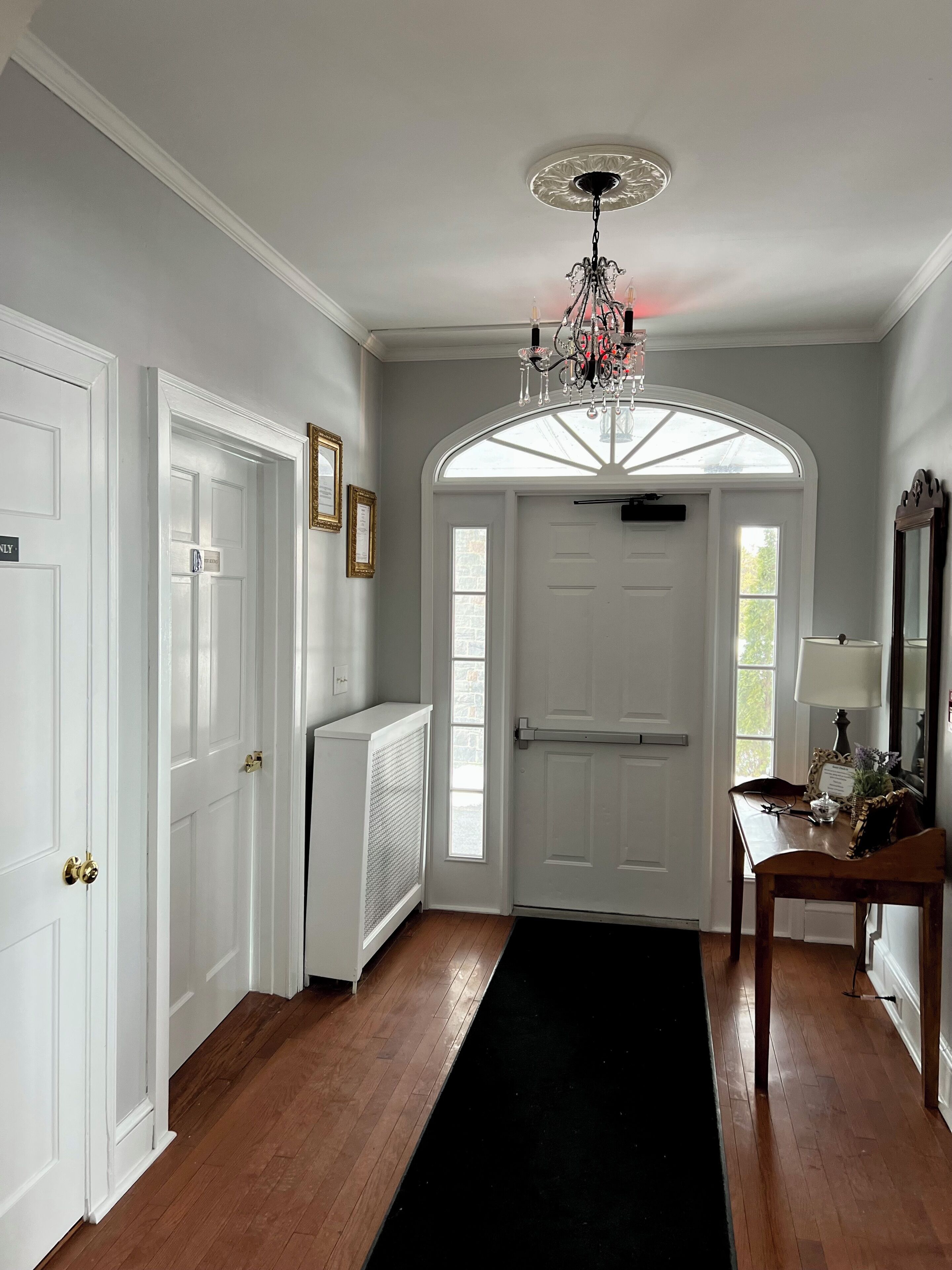 A hallway with white doors, a black carpet, and a chandelier.
