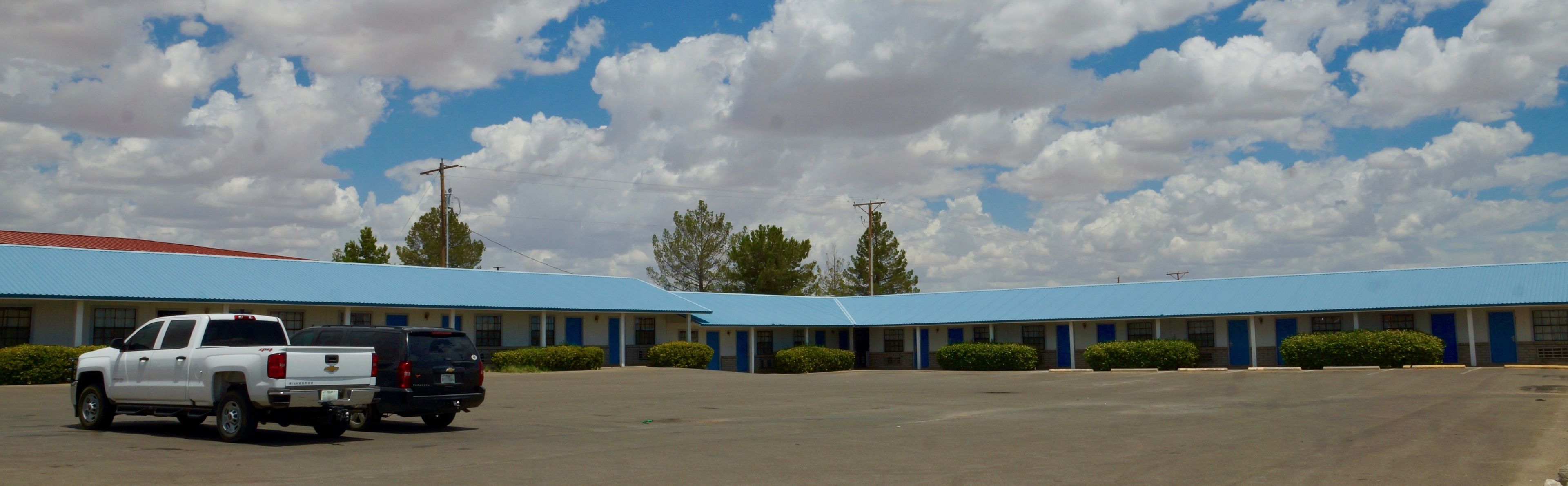 A motel with a blue roof and a parking lot.