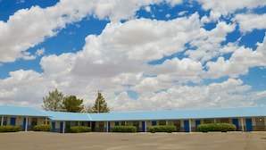 A motel with a blue roof and multiple rooms, a parking lot, and a clear sky with clouds. - Cotton Valley Motel (Clint)