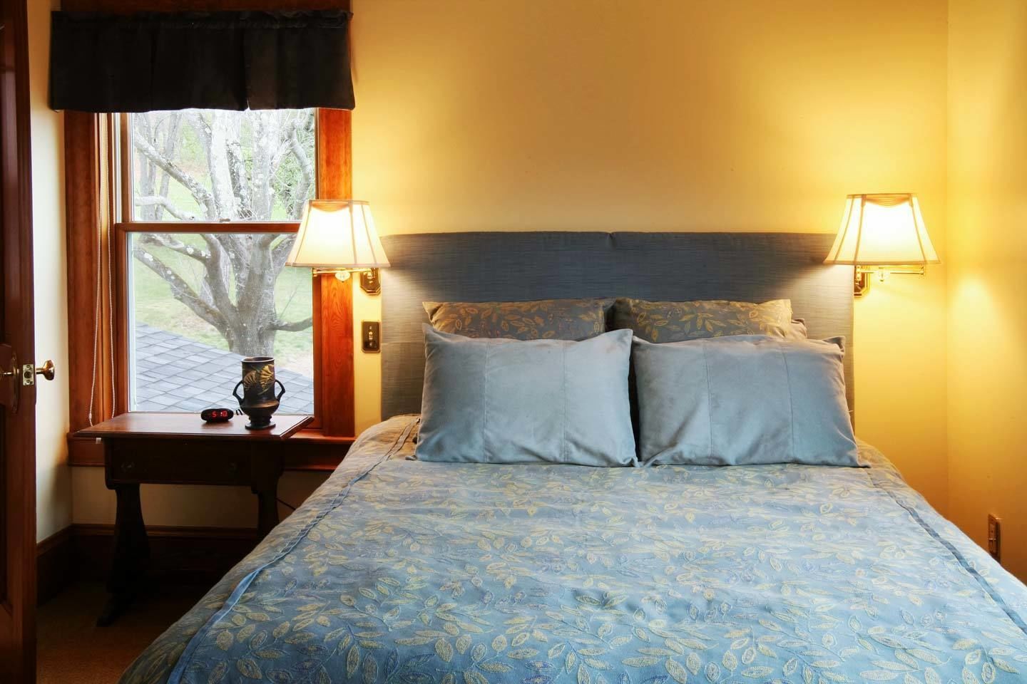 A bedroom with a bed, two bedside lamps, a nightstand, and a window with curtains.