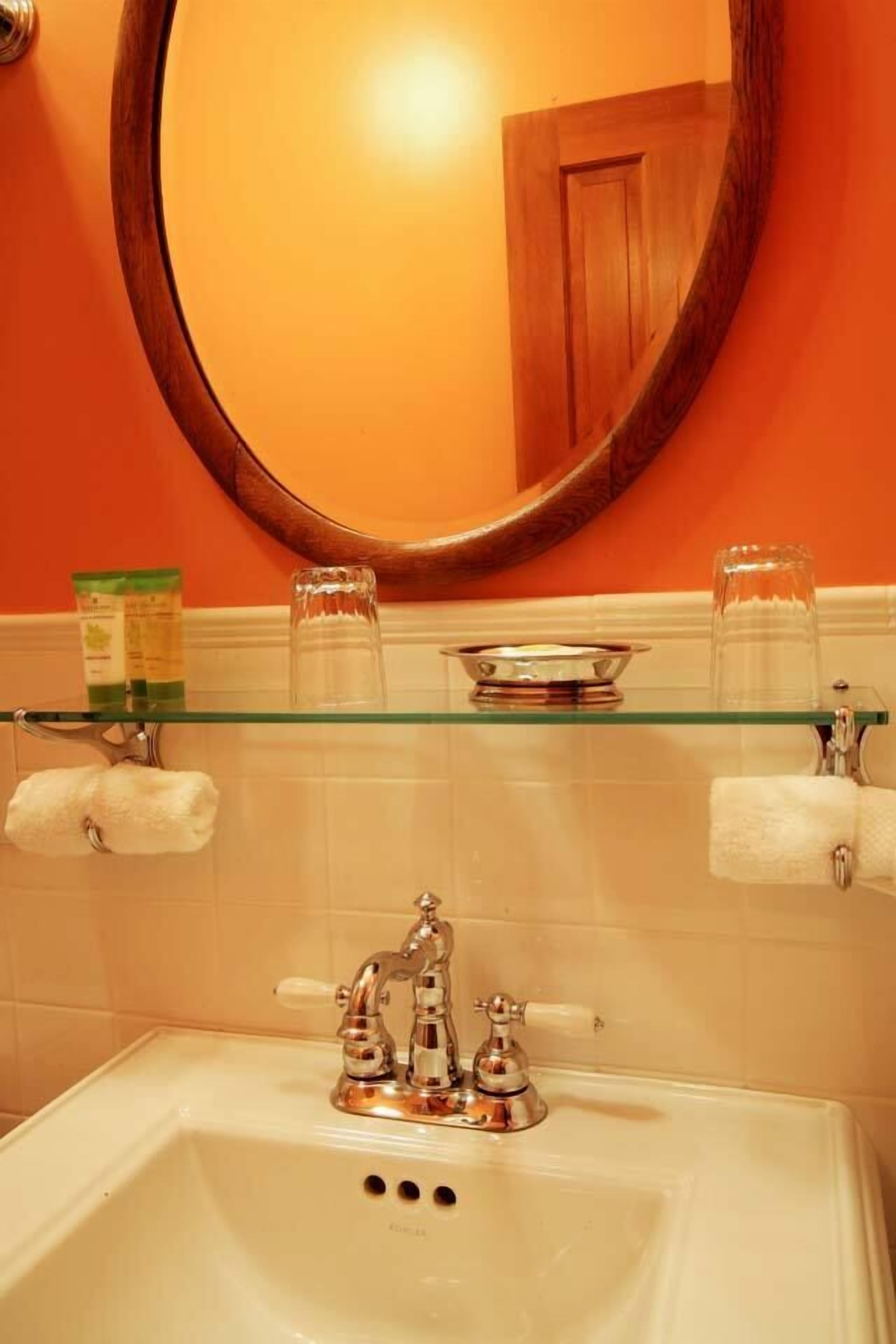 A bathroom with a white sink, two faucets, a glass shelf with toiletries, and a mirror on the wall.
