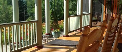 A covered porch with wooden chairs and a stone planter.