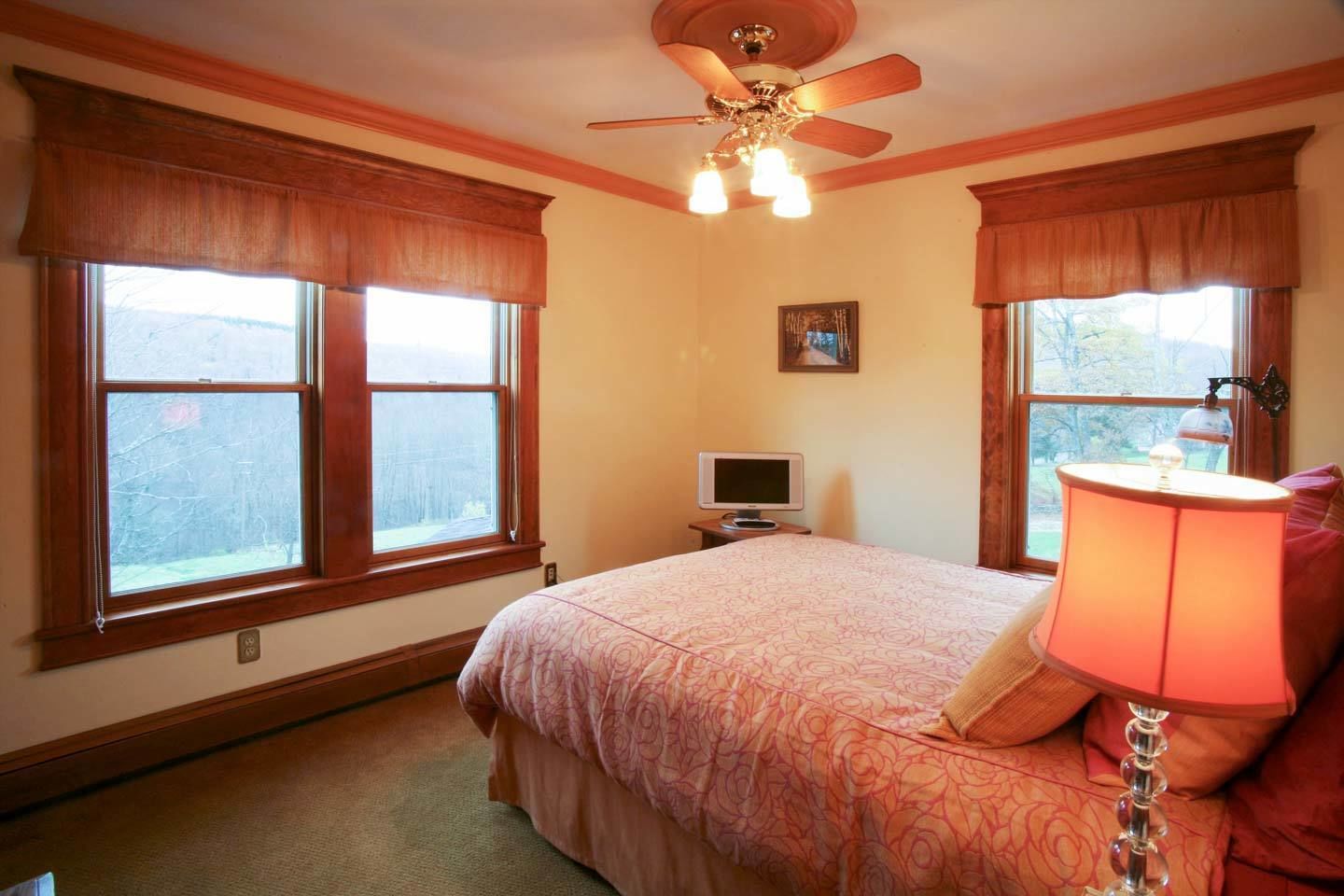 A bedroom with a bed, a ceiling fan, a television, and a lamp.