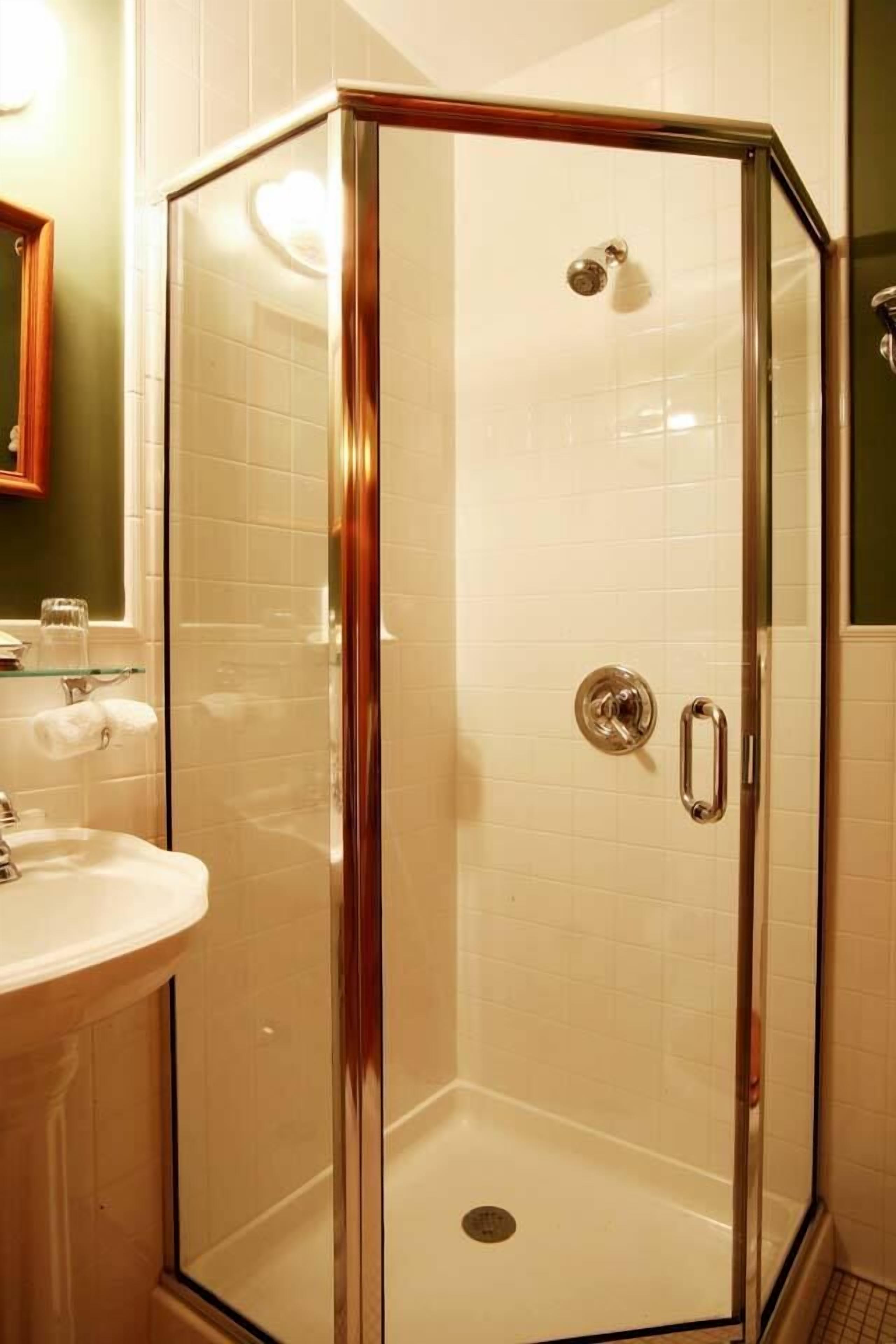 A glass-enclosed shower with a white tiled wall, a sink, and a mirror.