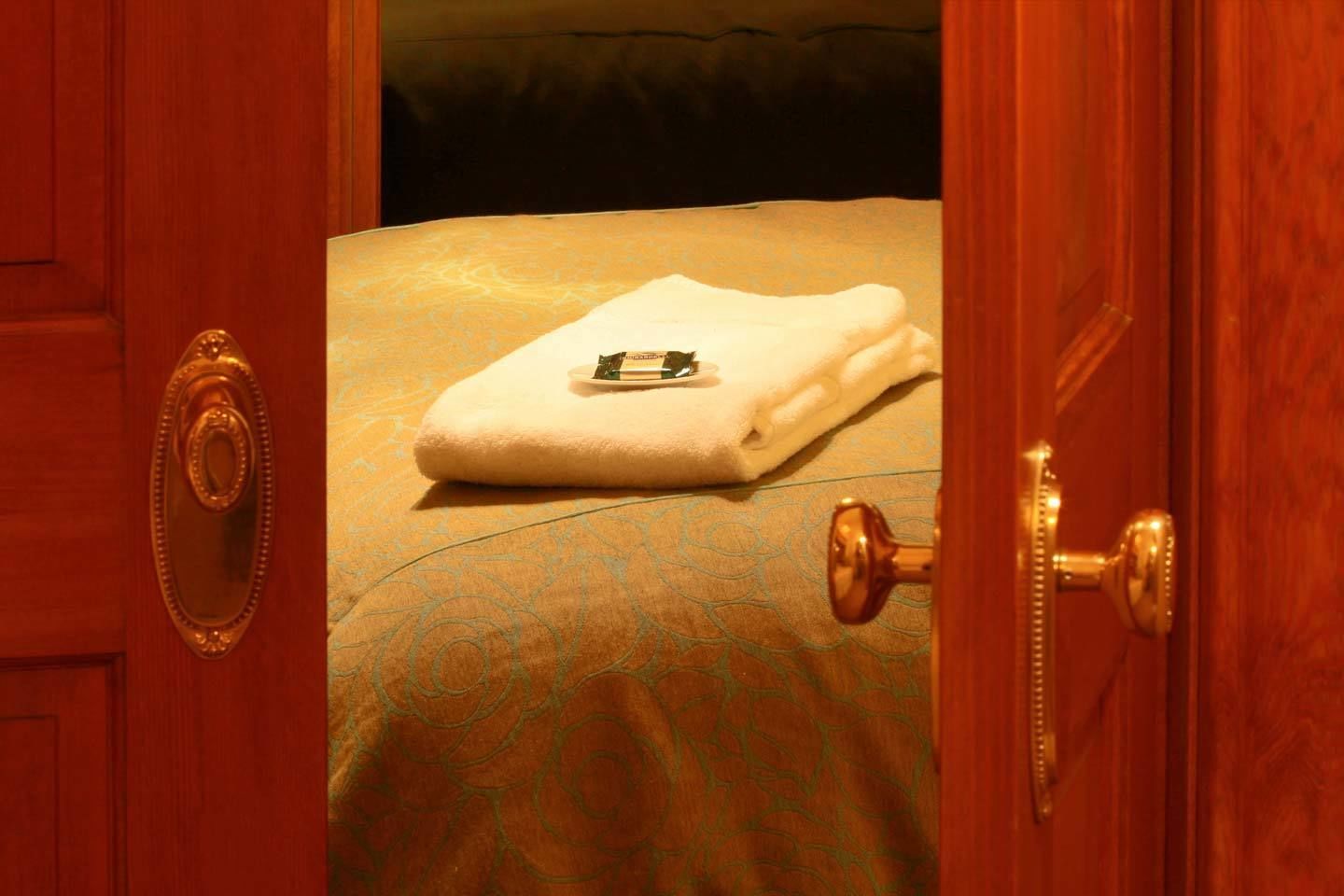 A hotel room with a bed, a neatly folded white towel, and a key on the bed.