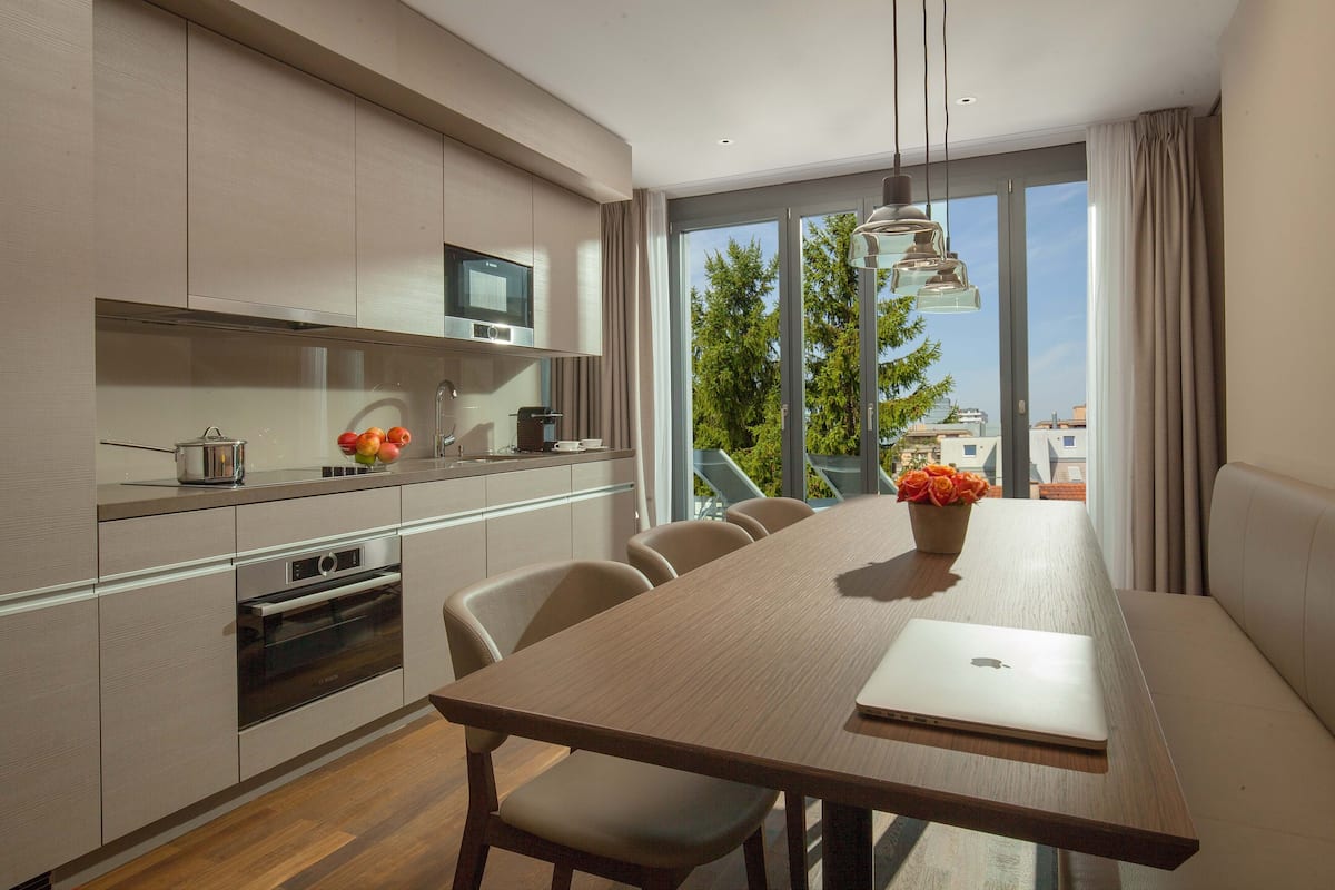 A modern kitchen with a dining area, a laptop on the table, and a view of the outdoors.