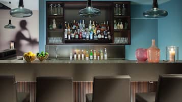 Zona de bar con diversas botellas de licores, un frutero y asientos.