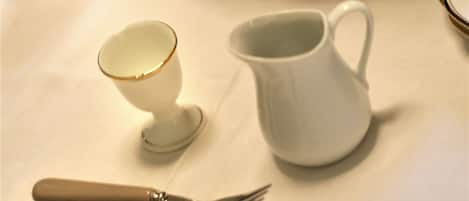 A table with a fruit basket, a small cup, a larger cup, and cutlery.
