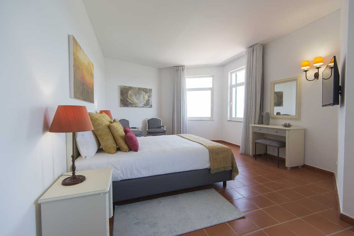 A bedroom with a bed, bedside table, lamp, and a desk with a chair.