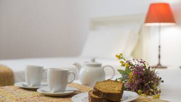 Een keurig opgemaakte ontbijttafel met een theepot, twee kopjes, een plakje taart en een vaas bloemen.