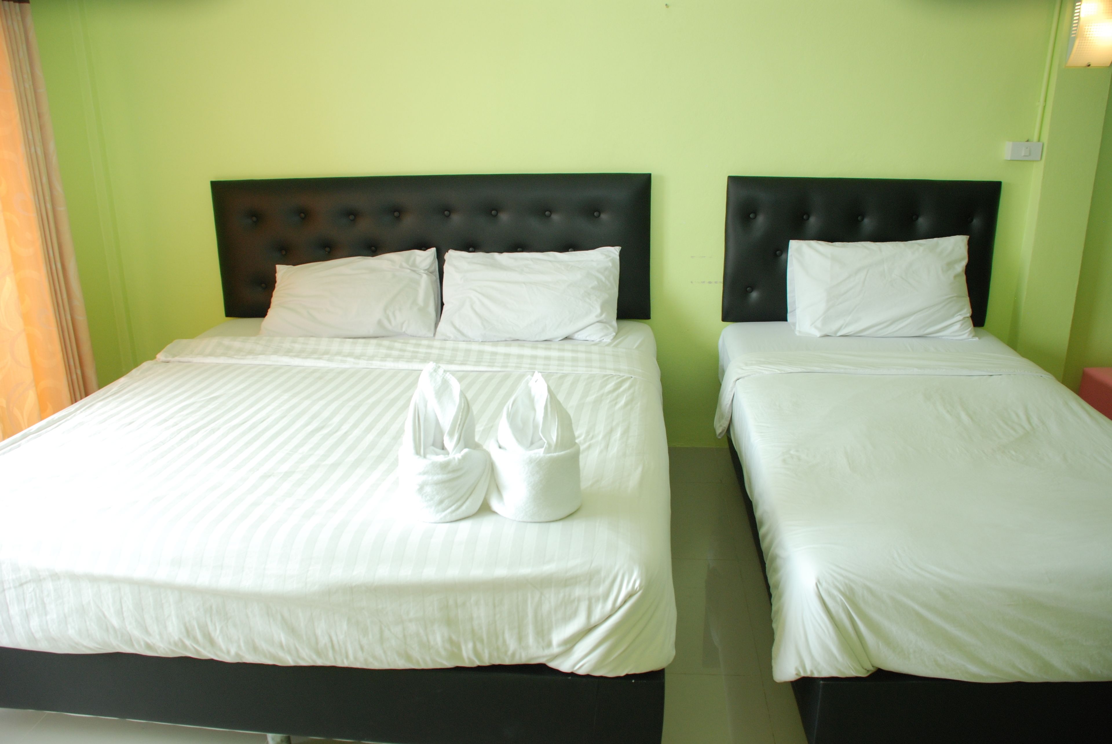 Dos camas individuales con cabeceros negros y ropa de cama blanca, incluyendo toallas sobre las camas.