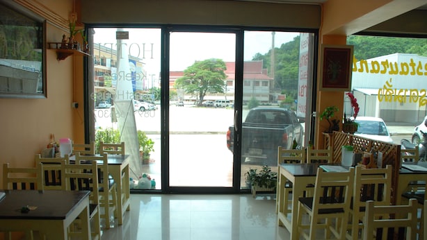 A restaurant interior with wooden tables and chairs, a large glass door leading outside, and various decorations including plants and wall art.