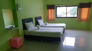 A hotel room with two beds, a glass table, a red ottoman, and a window with curtains.