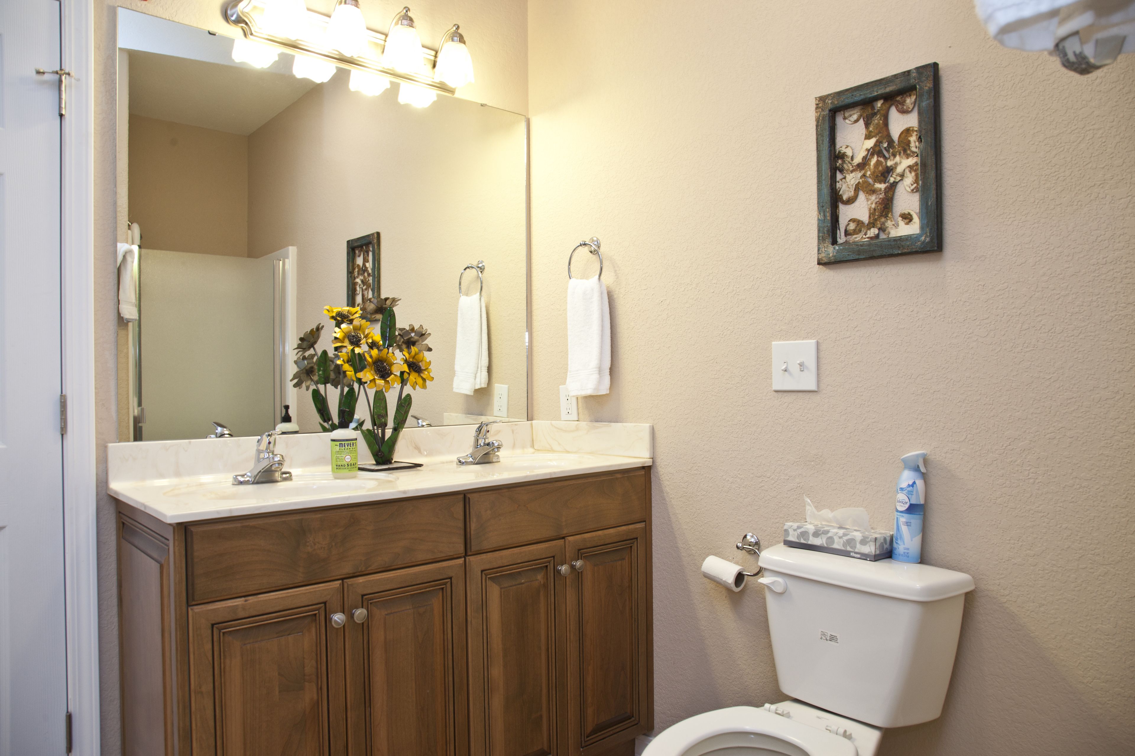 A bathroom with wooden cabinets, a white toilet, a sink with a mirror above it, and a framed picture on the wall.