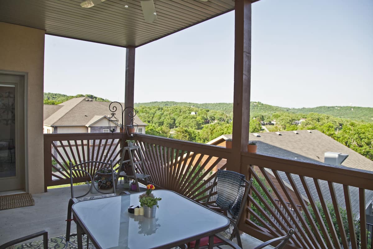 A covered balcony with a table and chairs, overlooking a green landscape.