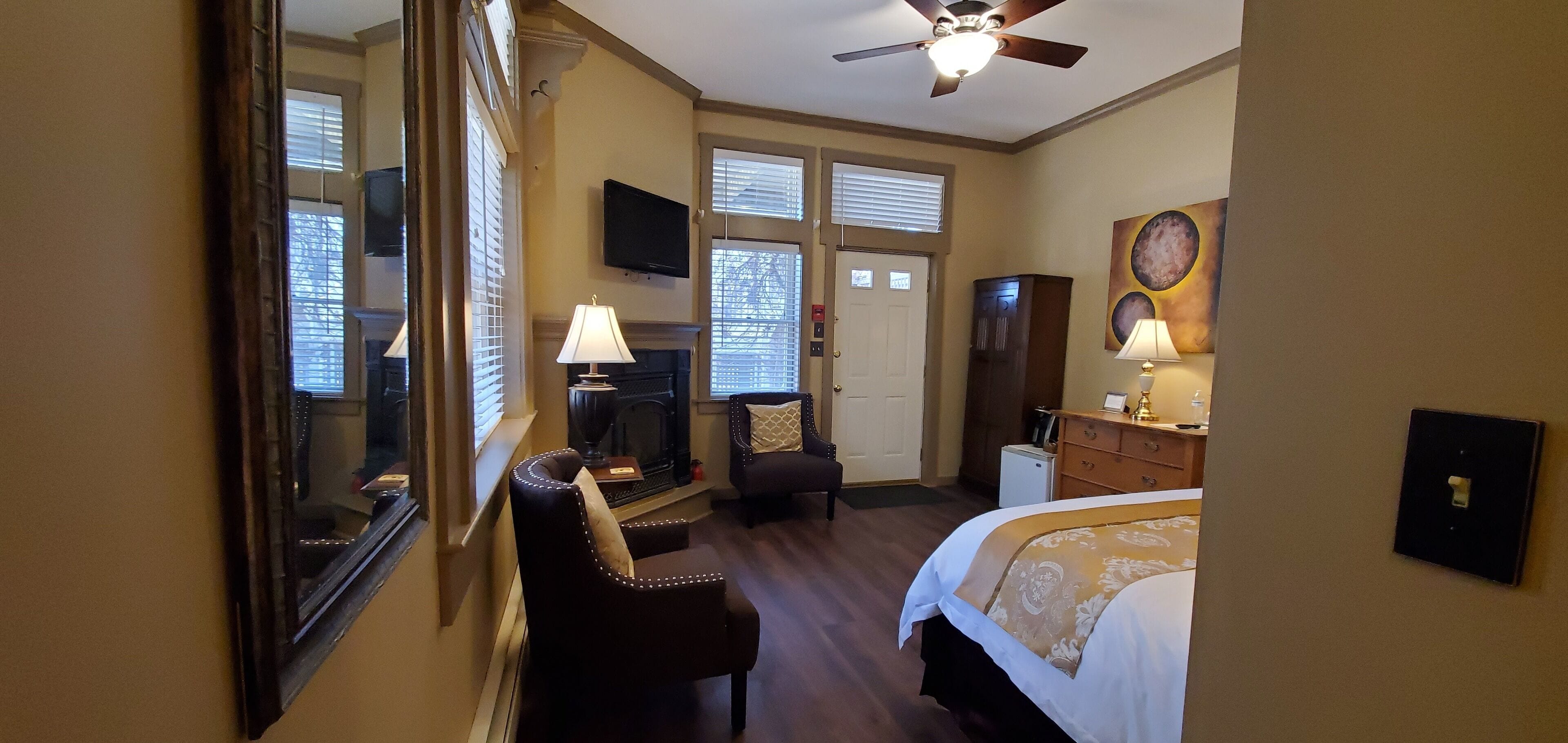 A hotel room with a bed, a desk, a chair, a television, and a fireplace.