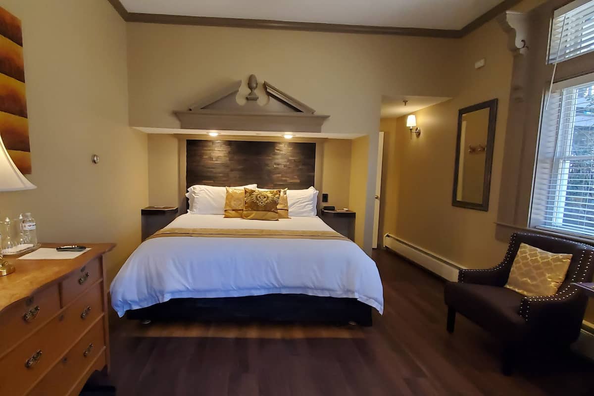 A hotel room with a bed, bedside tables, a dresser, a chair, and a window with blinds.