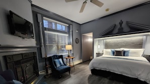 A modern hotel room with a fireplace, a large bed with a headboard, a TV mounted on the wall, and a ceiling fan. - Blackberry Inn (Camden)
