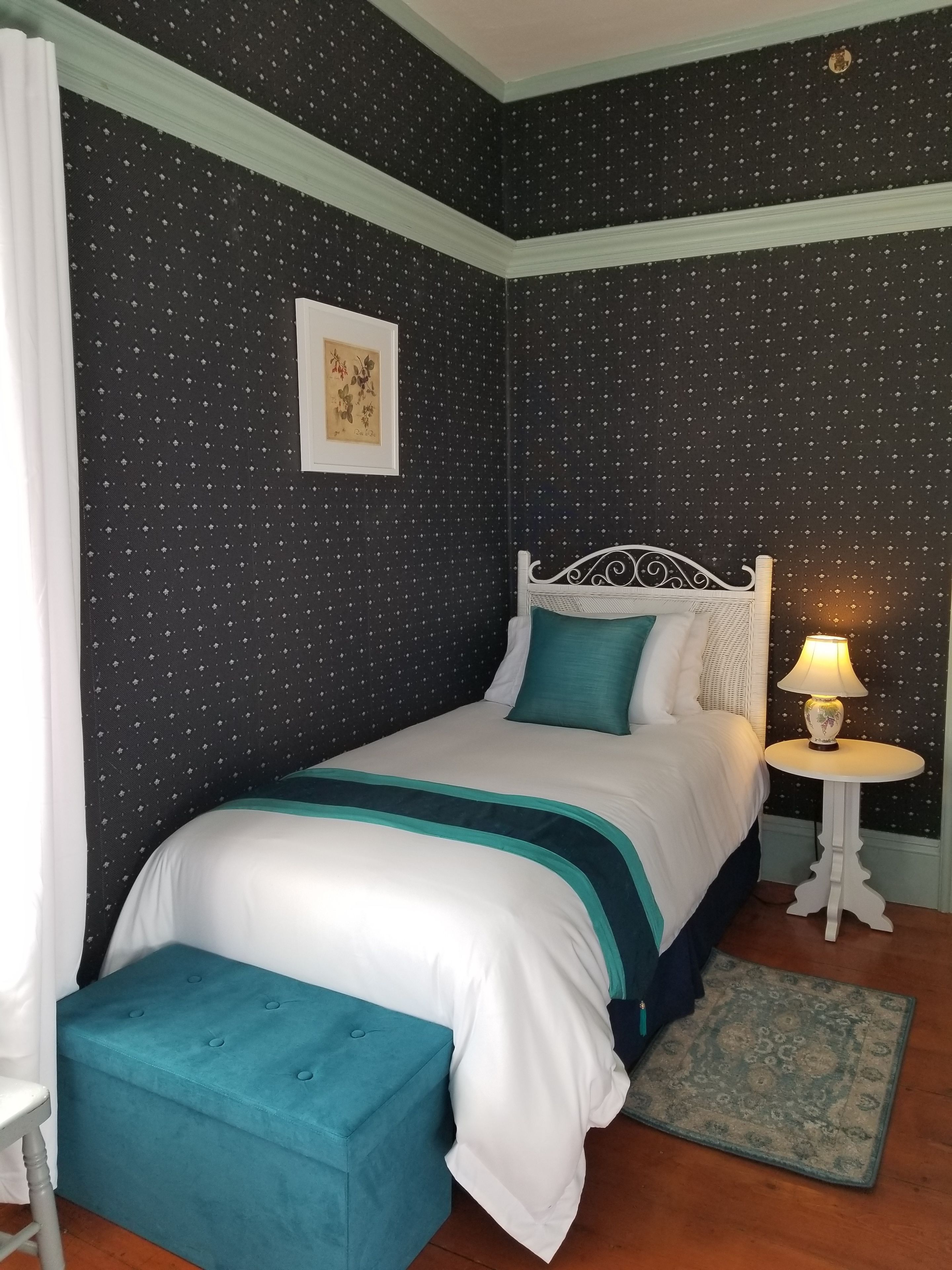 A neatly arranged bedroom with a bed, a bedside table with a lamp, a small rug, and a framed picture on the wall.