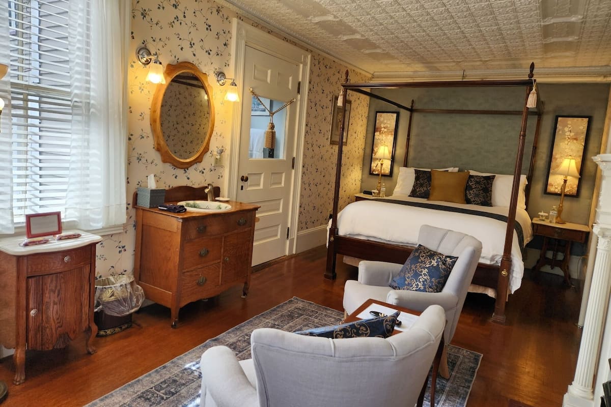 A bedroom with a four-poster bed, a wooden dresser, a round mirror, and a nightstand.