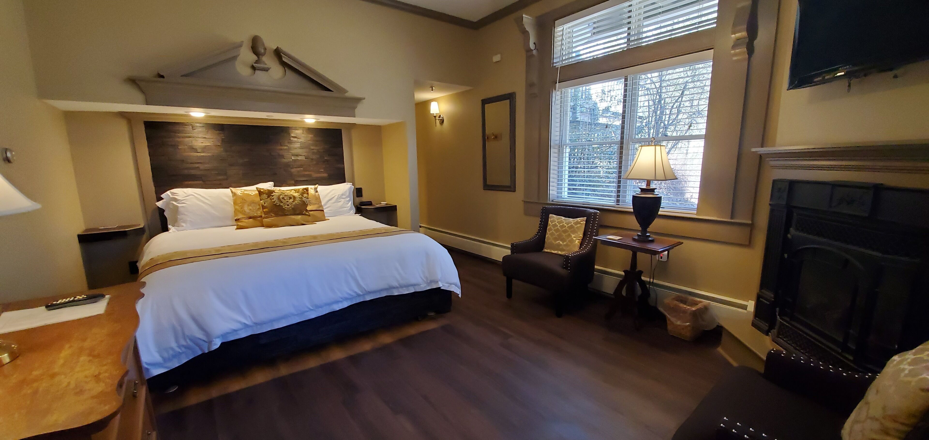Ein Hotelzimmer mit einem großen Bett, einem Kamin, einem Schreibtisch mit Lampe und einem Sessel.