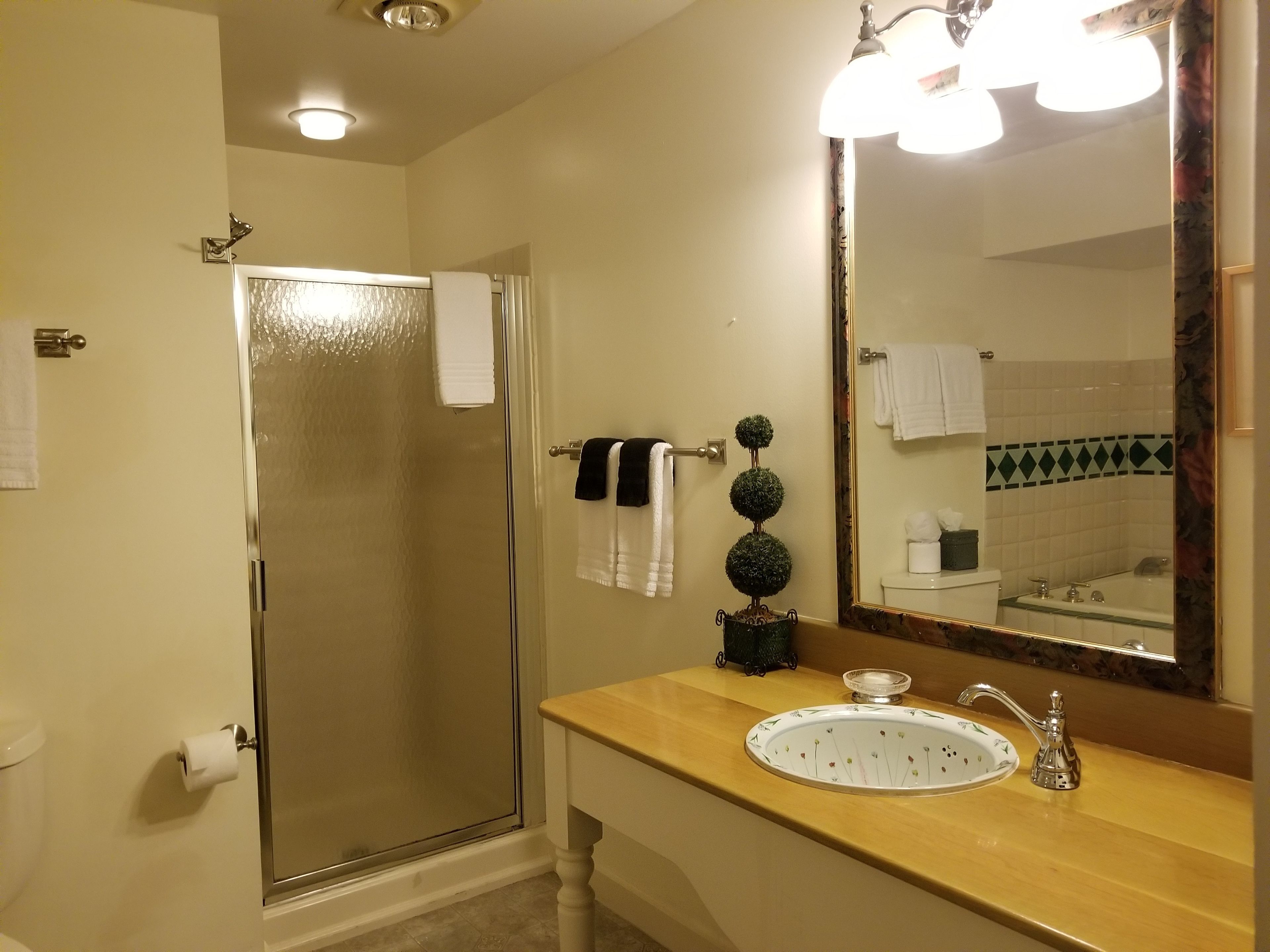 A bathroom with a glass shower door, a sink with a decorative mirror, and a toilet.