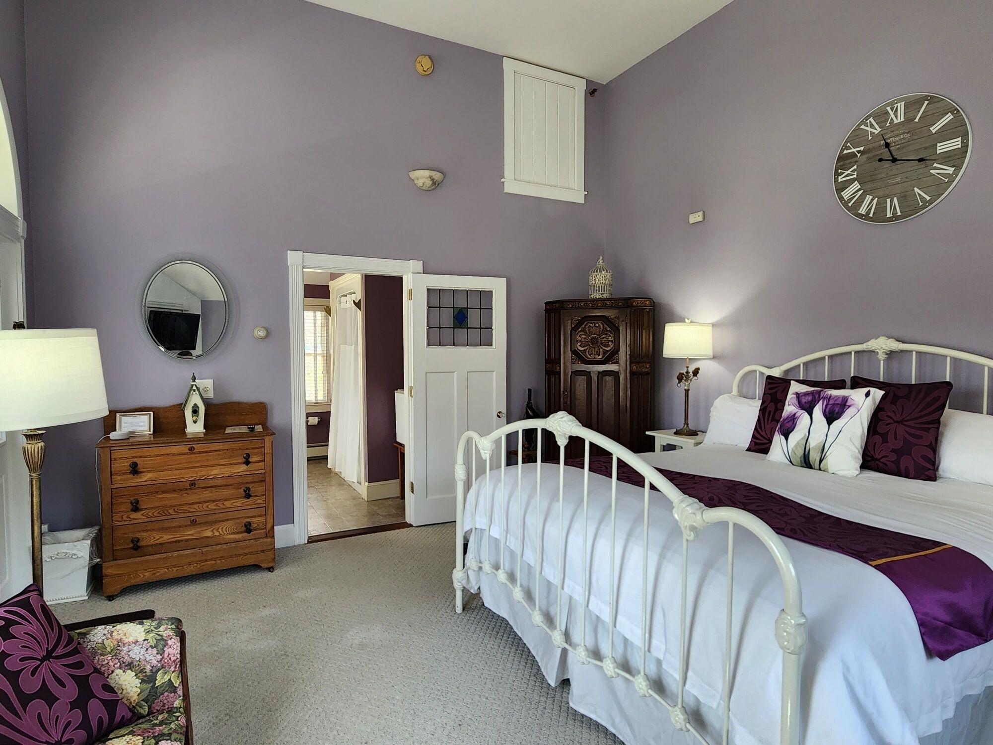 Un dormitorio con cama, cómoda, espejo y un reloj de pared.