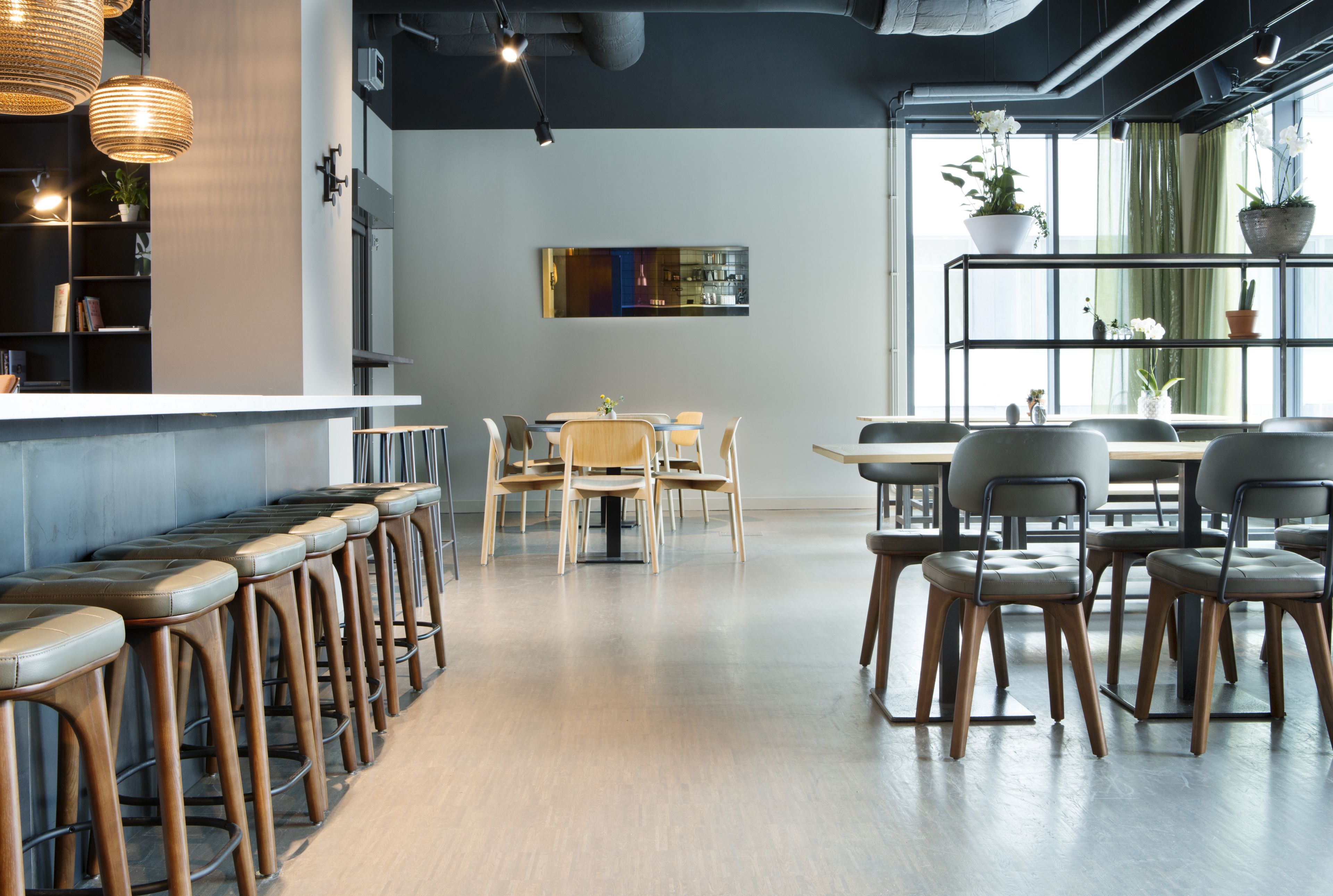 A modern bar area with wooden stools, a bar counter, and a seating area with tables and chairs.