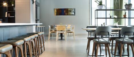A modern bar area with wooden stools, a bar counter, and a seating area with tables and chairs.