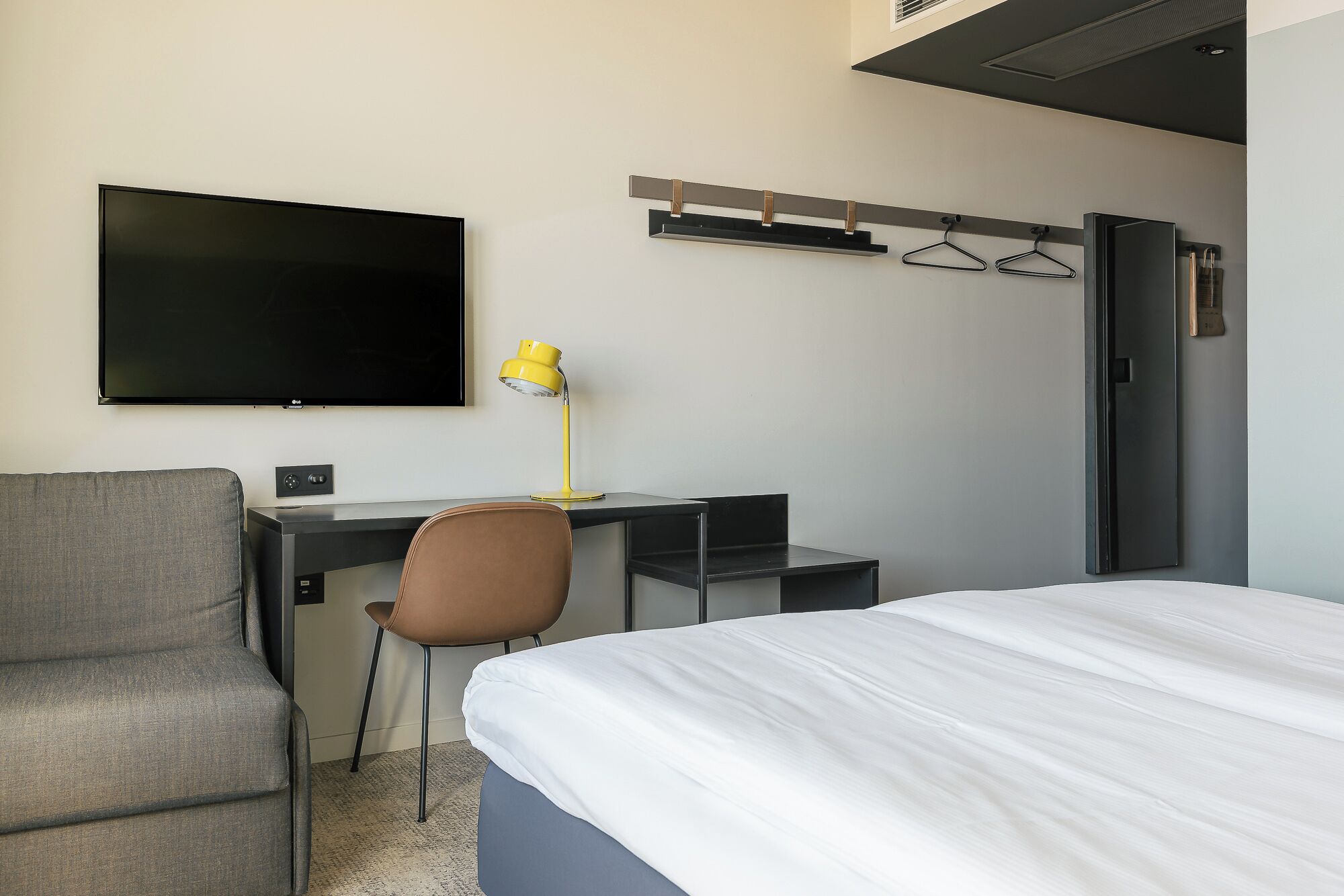 Una habitación de hotel con una cama, un escritorio, una silla, un televisor y un perchero.