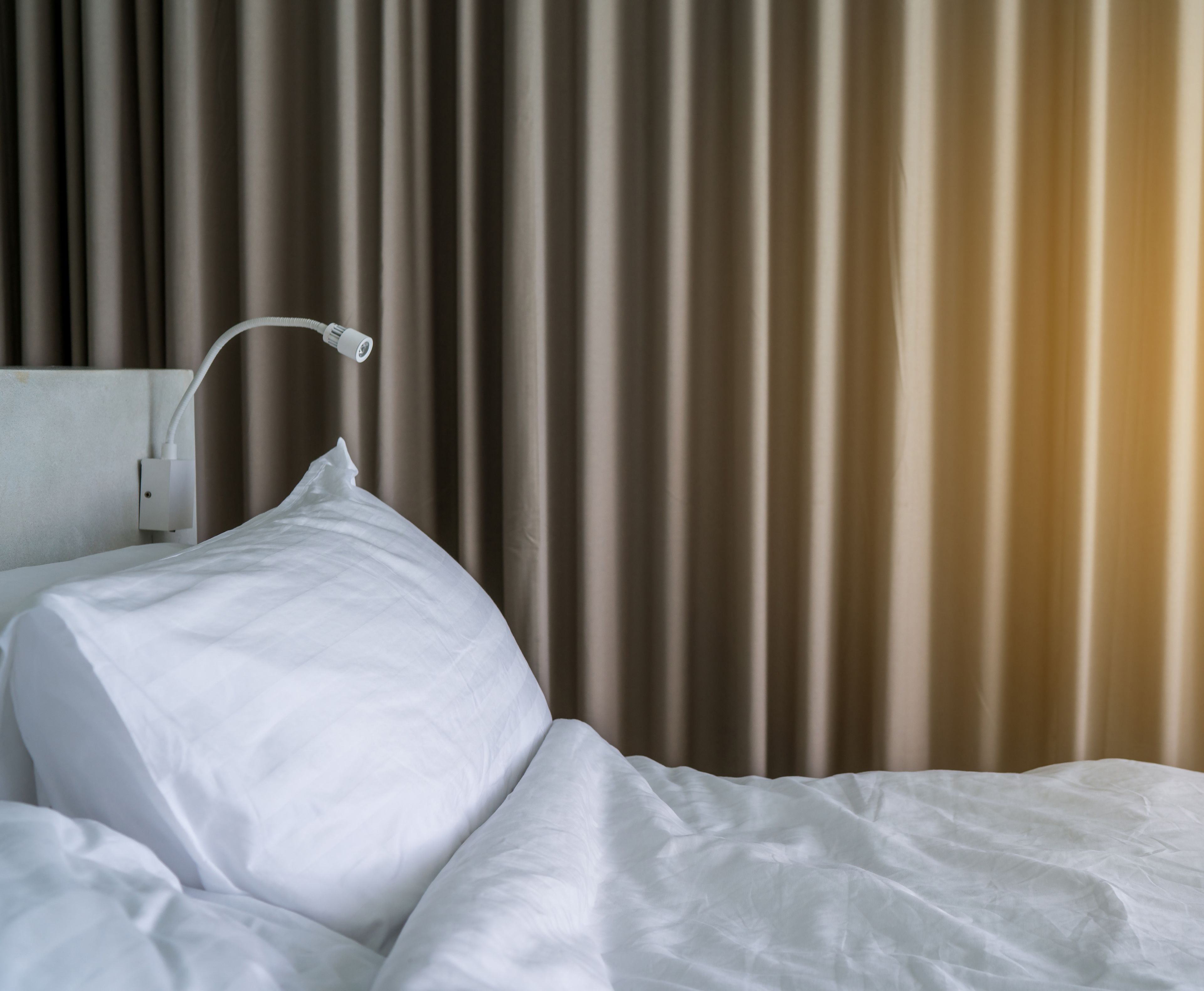 A neatly made bed with white linens and a white headboard.