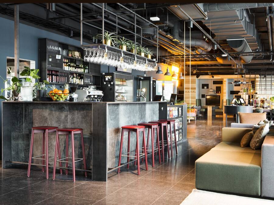 Un área de bar moderna con taburetes, una barra y estantes llenos de botellas y vasos.
